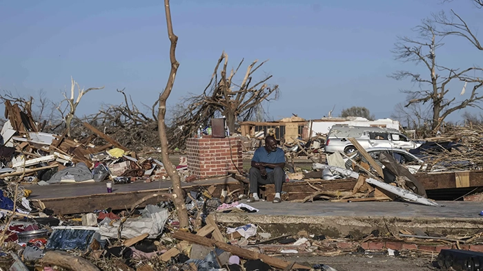 A man is sitting on the remains of a house that was destroyed by a tornado.