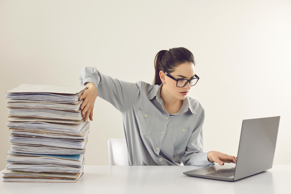 Young accountant working on laptop sitting on desk with arm leaning on a stack of papers